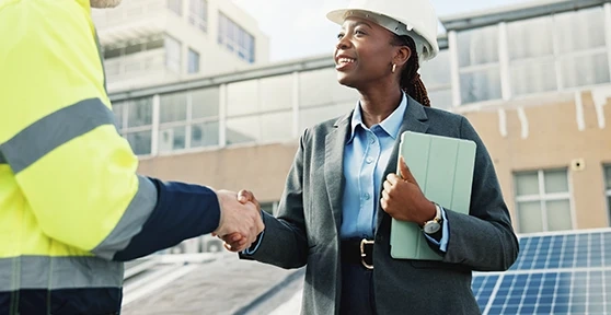 Woman in a suit and hard hat shakes hands with a worker on a building site