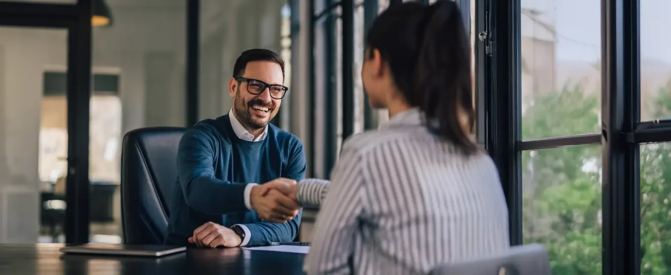 Homem e mulher a apertar as mãos numa mesa de escritório