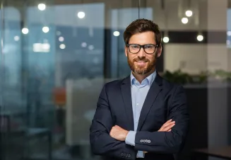 Homem com óculos, vestido com uma camisa e blazer, de braços cruzados