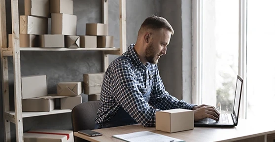 Man working on a laptop in an office with parcel boxes