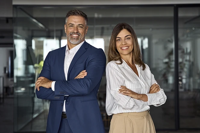 Homem e mulher de negócios sorriem com os braços cruzados num escritório