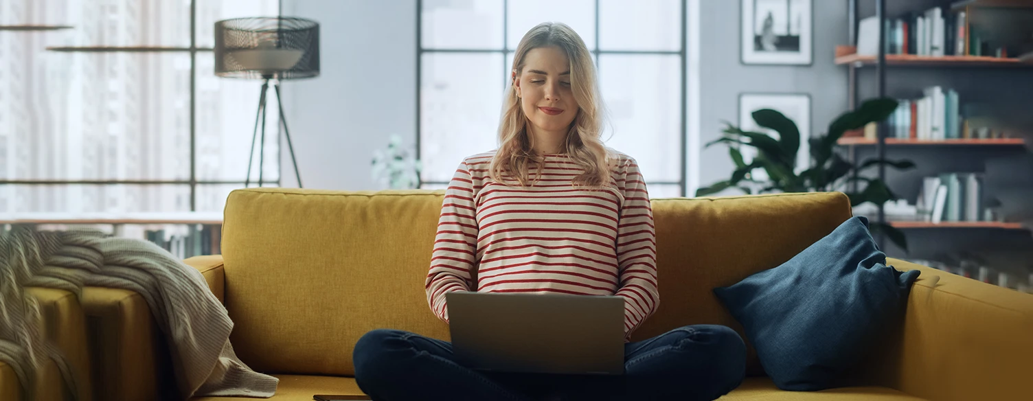 woman sitting with crossed legs on sofa, working on laptop