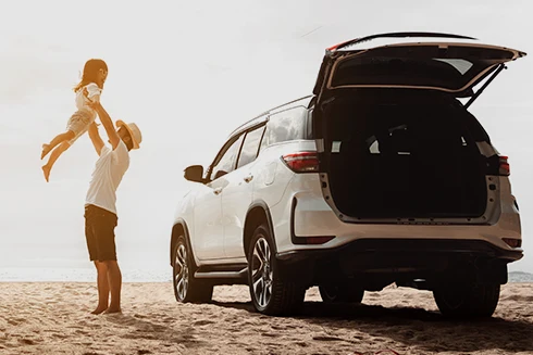 man lifting his daughter in his arms, next to his new car