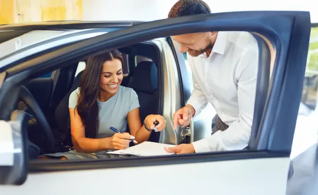 Mulher a assinar documentos dentro de um carro novo com vendedor ao lado