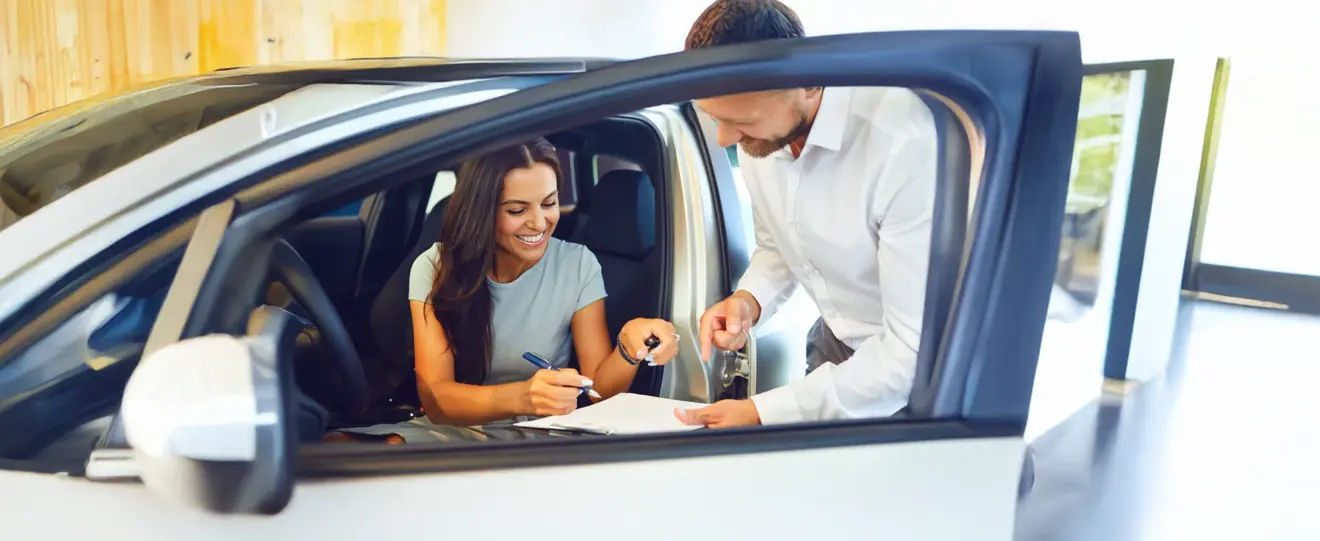 Mulher a assinar documentos dentro de um carro novo com vendedor ao lado