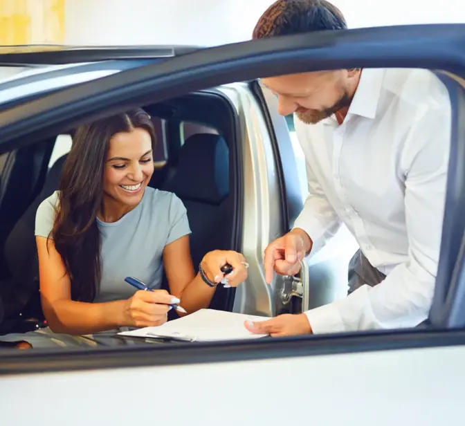 Mulher a assinar documentos dentro de um carro novo com vendedor ao lado