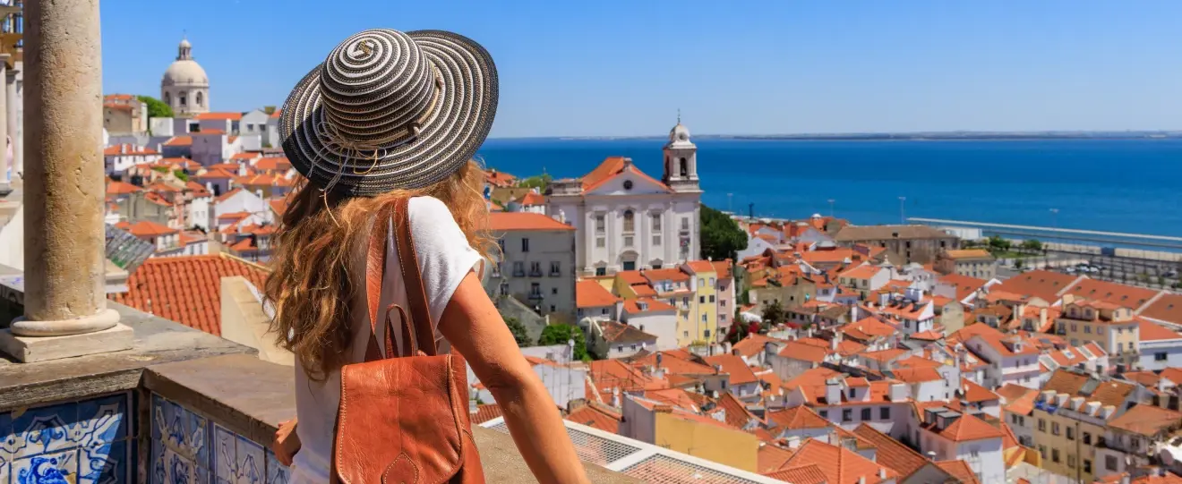 Mulher de costas com chapéu observa a vista panorâmica sobre a cidade de Lisboa e o rio