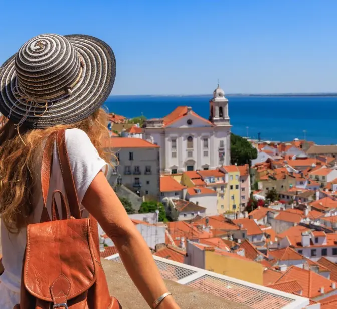 Mulher de costas com chapéu observa a vista panorâmica sobre a cidade de Lisboa e o rio