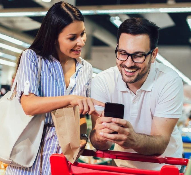 Casal sorridente a usar o telemóvel enquanto faz compras no supermercado