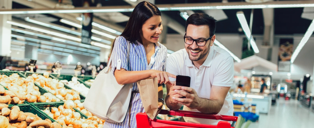 Casal sorridente a usar o telemóvel enquanto faz compras no supermercado