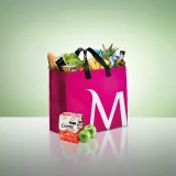 Saco de compras cerise, com o "M" de Millennium bcp desenhado, cheio de fruta, legumes e outra comida