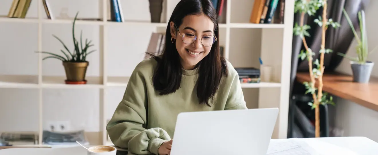 Jovem mulher sorridente a trabalhar num portátil com café na secretária