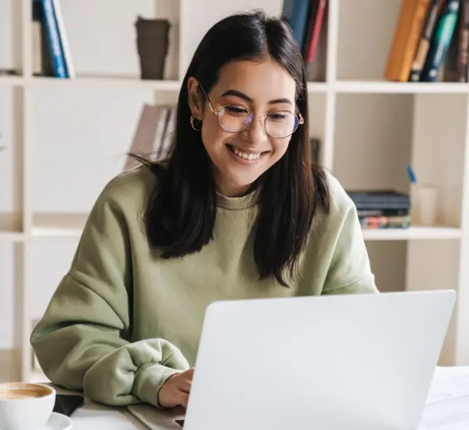 Jovem mulher sorridente a trabalhar num portátil com café na secretária
