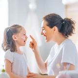 Senhora e criança a sorrirem e a porem creme na cara