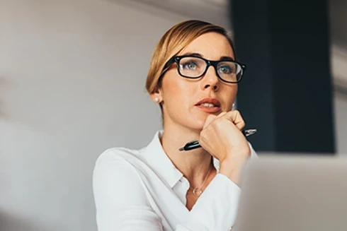 senhora em frente a computador, com caneta na mão
