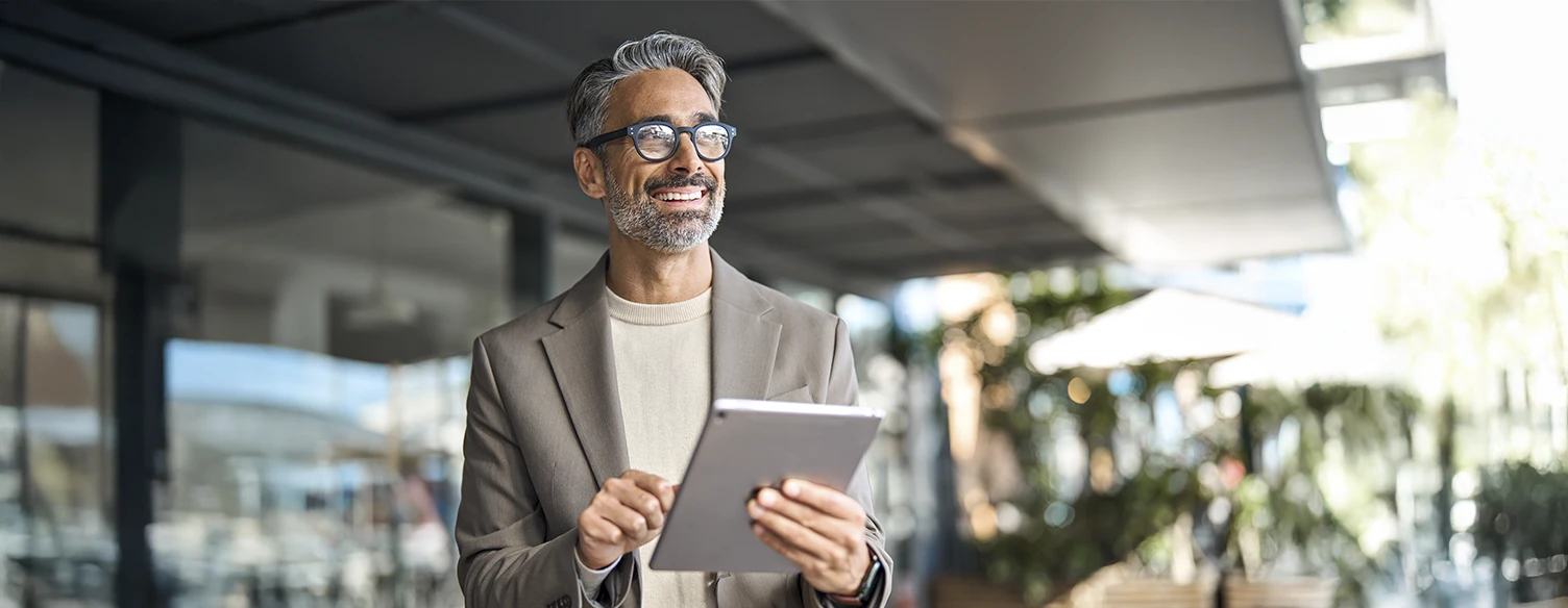 Grey-haired man with glasses, outside a building, holding a tablet