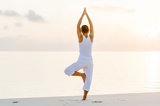 Mulher a fazer yoga na praia, ao pôr do sol