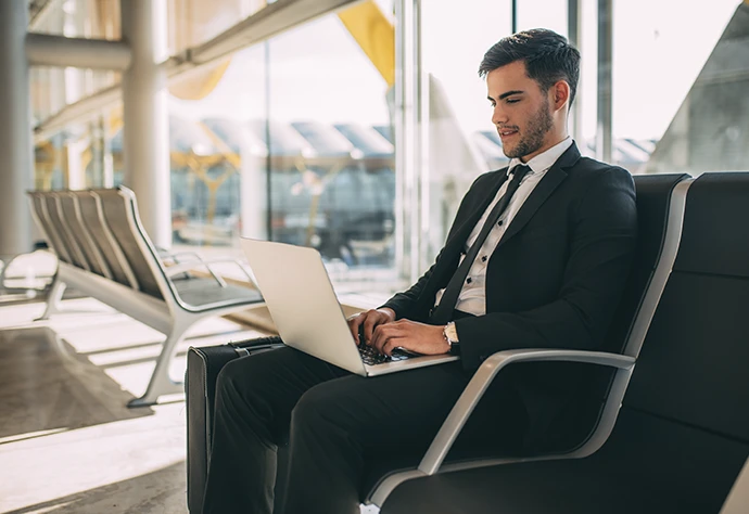 homem de fato sentado num aeroporto, com computador ao colo