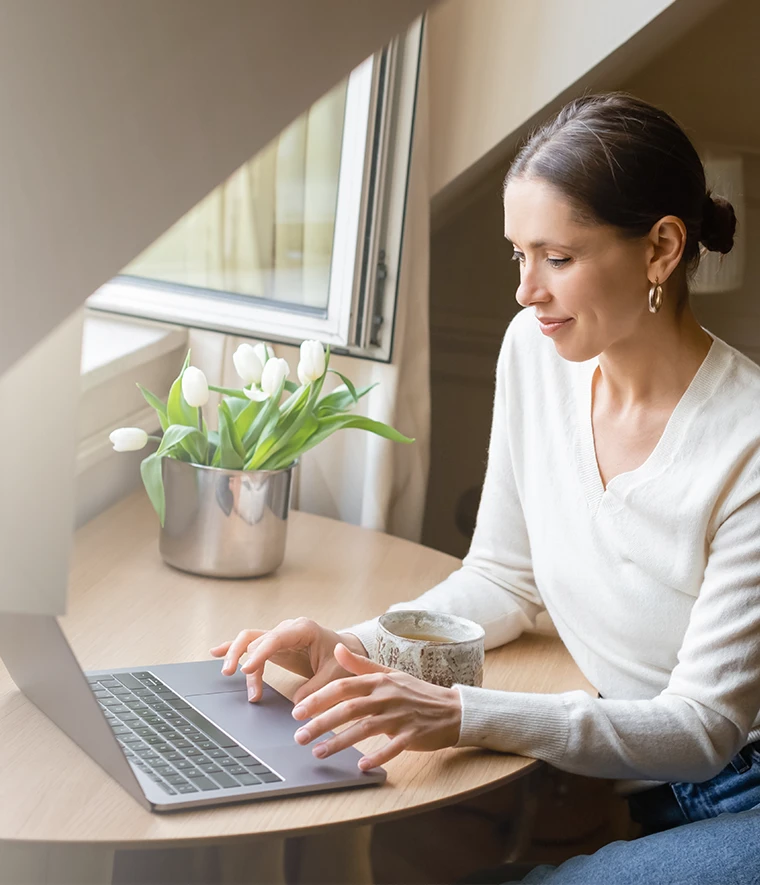 mulher sentada numa secretária à janela, a trabalhar no computador
