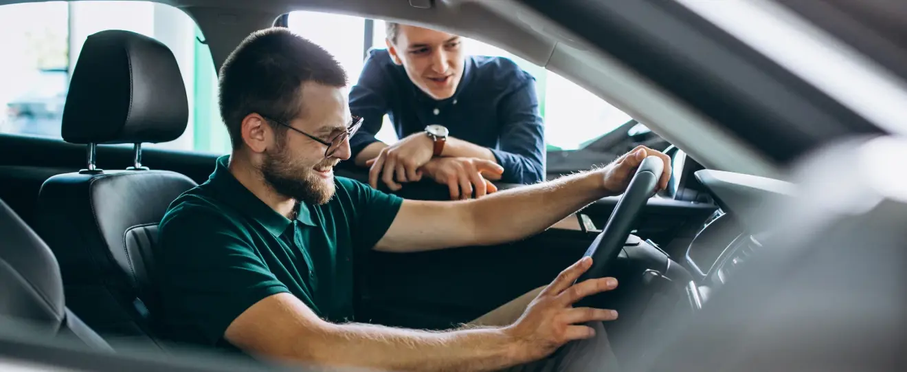 Homem a testar carro novo com vendedor a dar explicações
