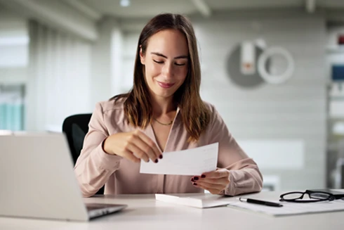 senhora sorridente num escritório, com carta cheque na mão