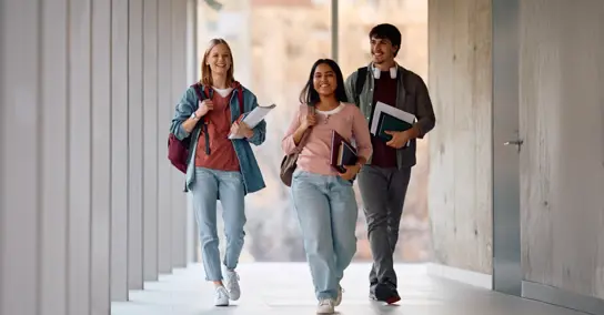 Três estudantes sorridentes a caminhar num corredor moderno