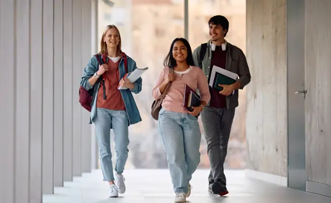 Três estudantes sorridentes a caminhar num corredor moderno