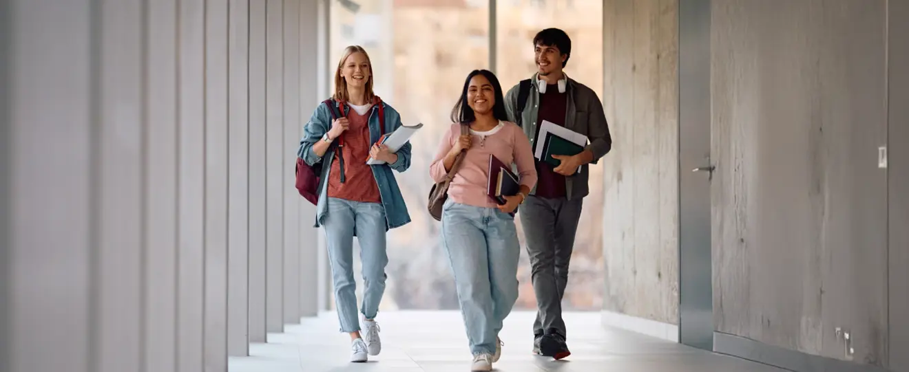 Três estudantes sorridentes a caminhar num corredor moderno