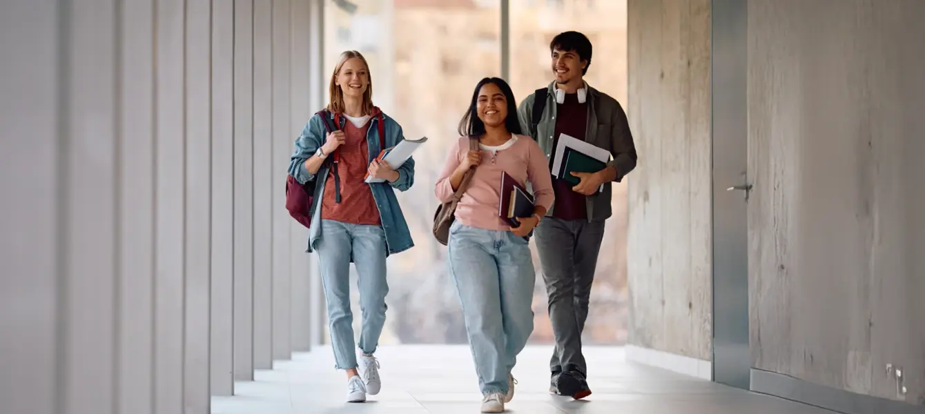 Três estudantes sorridentes a caminhar num corredor moderno
