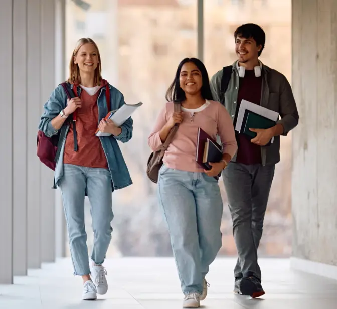 Três estudantes sorridentes a caminhar num corredor moderno