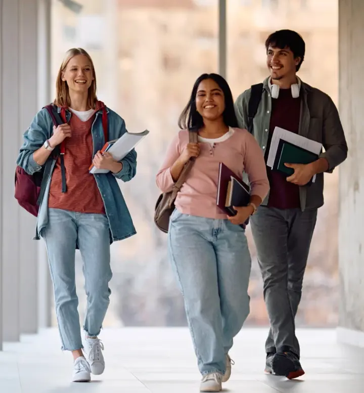Três estudantes sorridentes a caminhar num corredor moderno