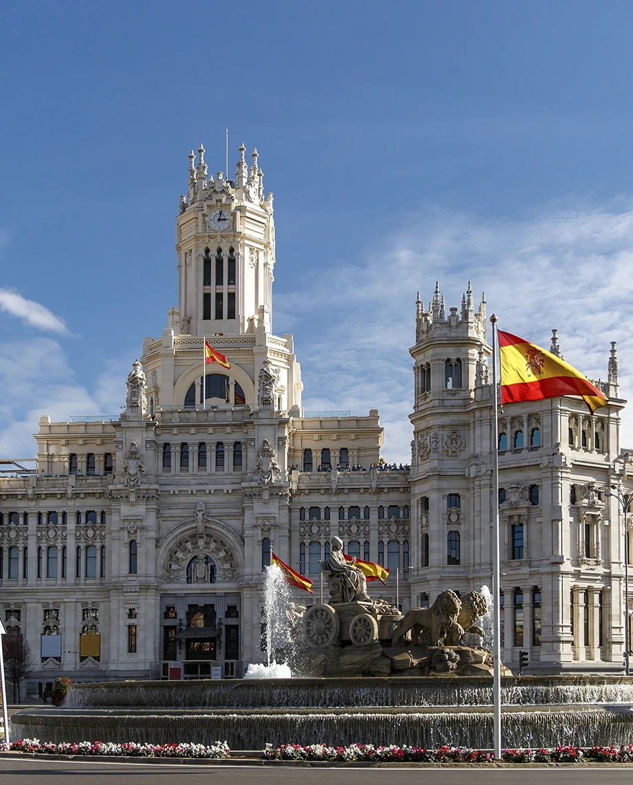 Cybele Palace and fountain in Madrid with Spanish flags under a blue sky