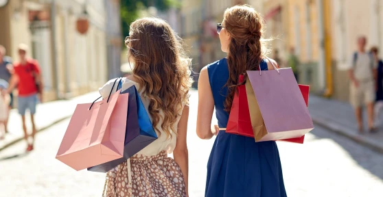 Duas mulheres vistas de costas com sacos de compras numa rua
