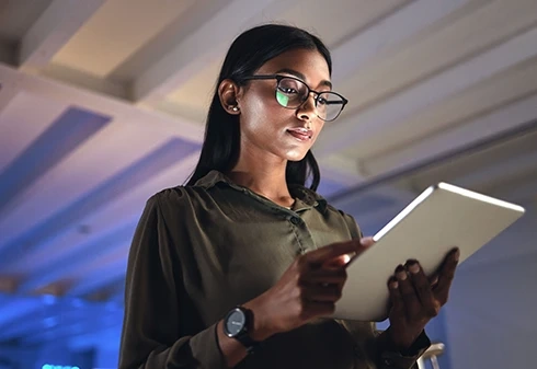 Mulher de óculos a utilizar um tablet num ambiente com pouca luz