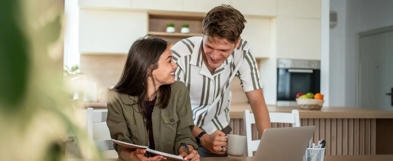 Casal jovem conversa sobre o orçamento familiar na cozinha, usando um computador portátil