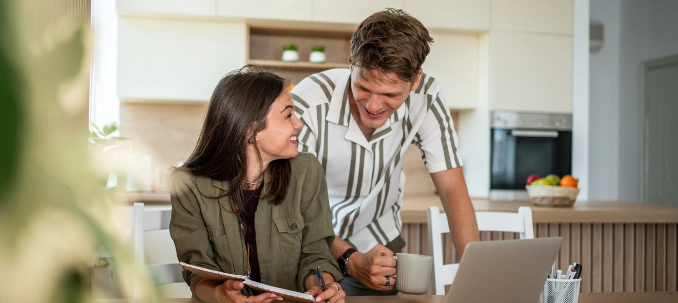 Casal jovem conversa sobre o orçamento familiar na cozinha, usando um computador portátil
