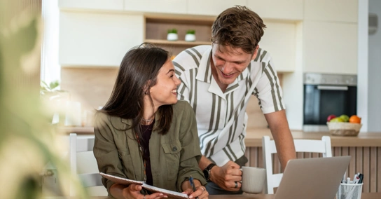 Casal jovem conversa sobre o orçamento familiar na cozinha, usando um computador portátil