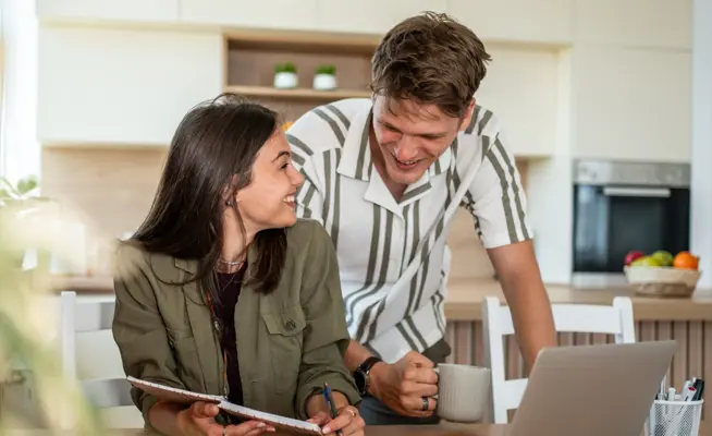 Casal jovem conversa sobre o orçamento familiar na cozinha, usando um computador portátil