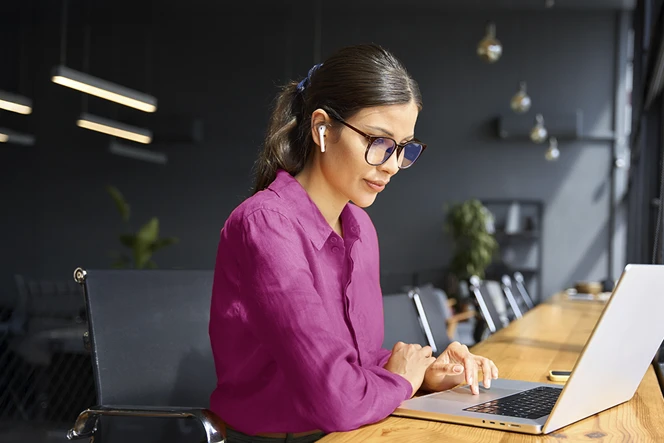 Woman sitting with a long wooden table in front of her, where she has her computer