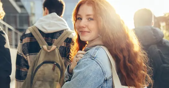 Jovem ruiva sorridente a olhar para a câmara, com estudantes atrás
