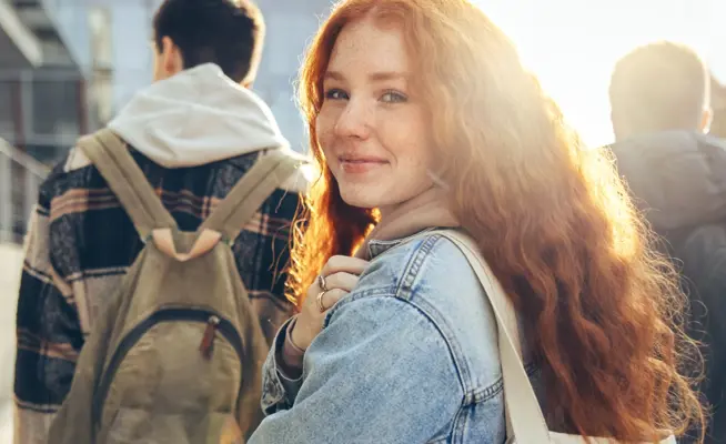 Jovem ruiva sorridente a olhar para a câmara, com estudantes atrás