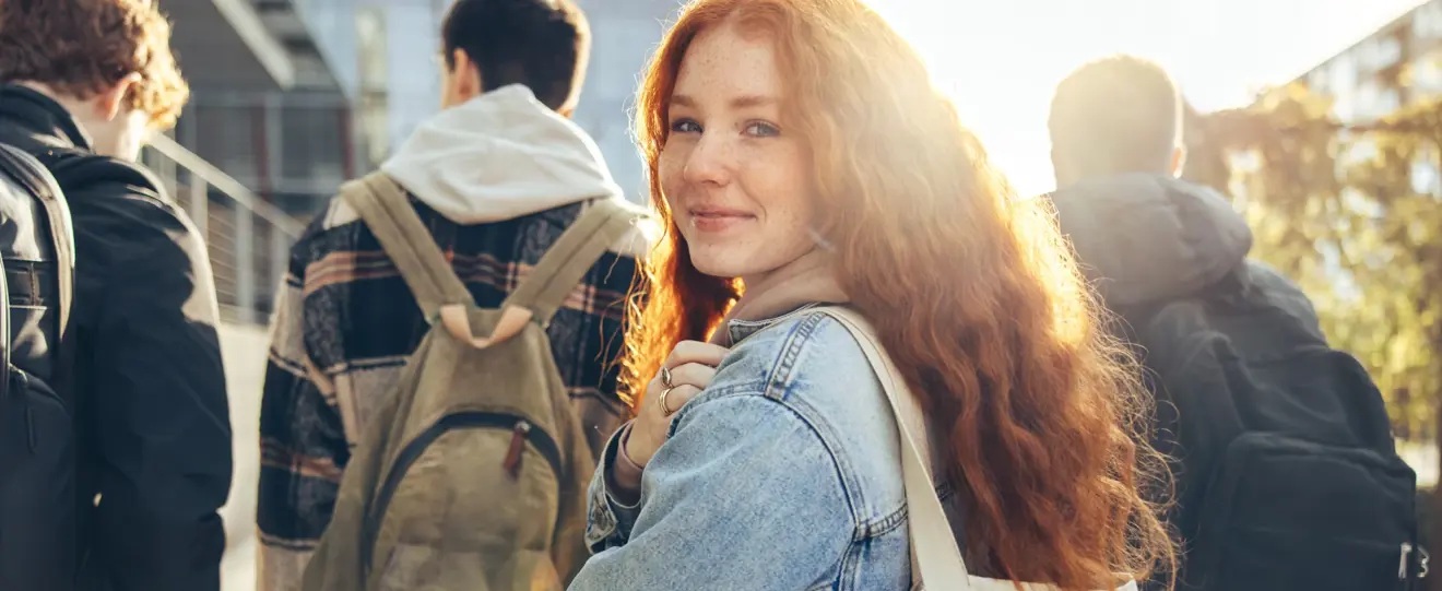 Jovem ruiva sorridente a olhar para a câmara, com estudantes atrás