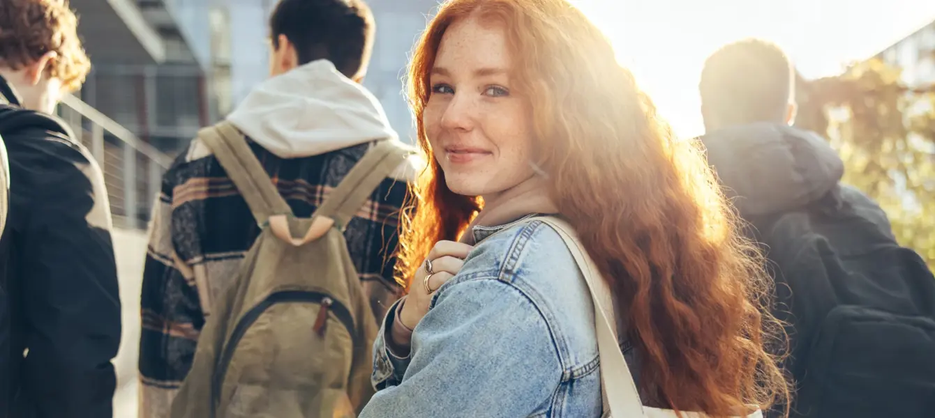 Jovem ruiva sorridente a olhar para a câmara, com estudantes atrás