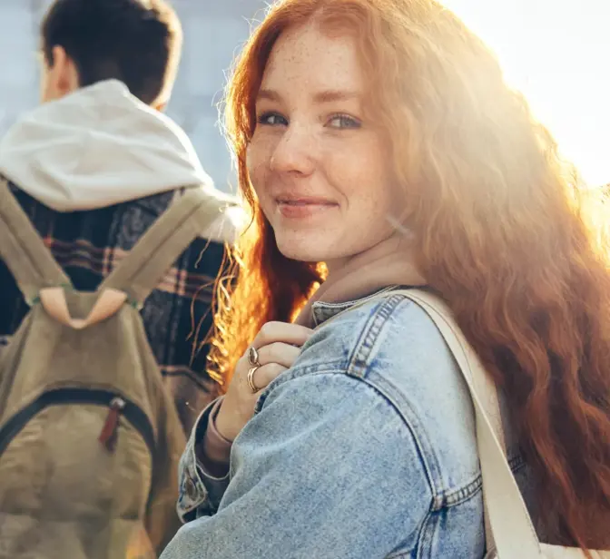 Jovem ruiva sorridente a olhar para a câmara, com estudantes atrás