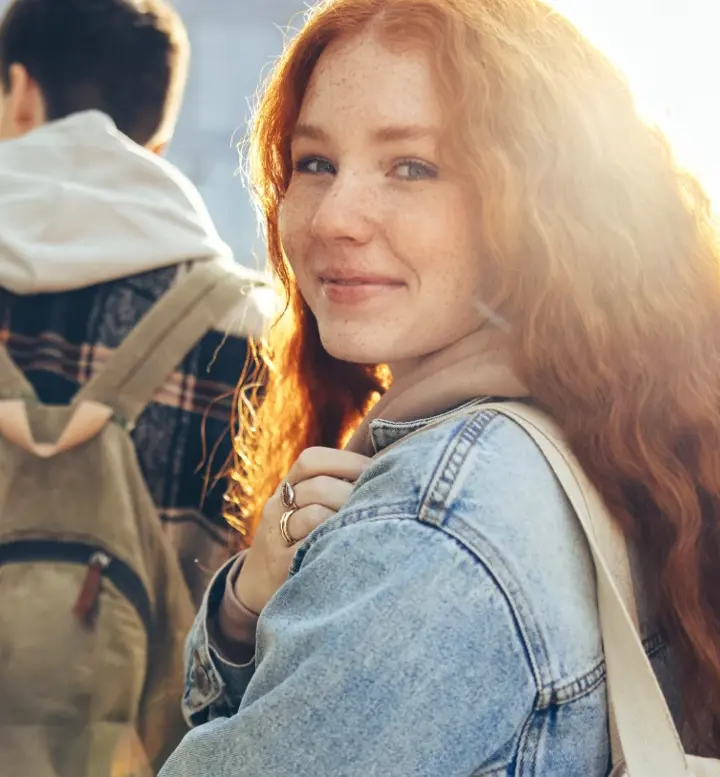 Jovem ruiva sorridente a olhar para a câmara, com estudantes atrás