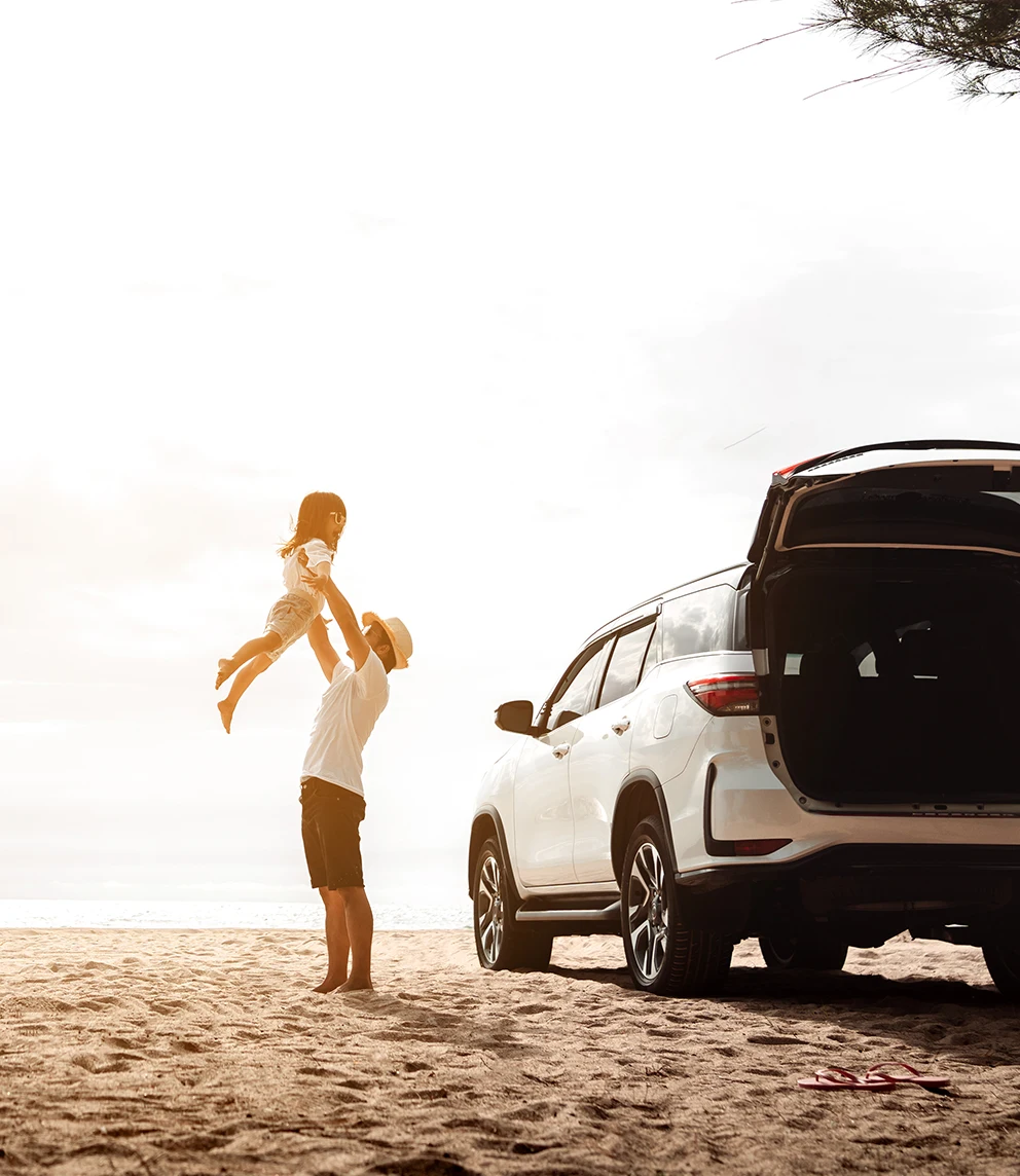 man lifting his daughter in his arms, next to his new car