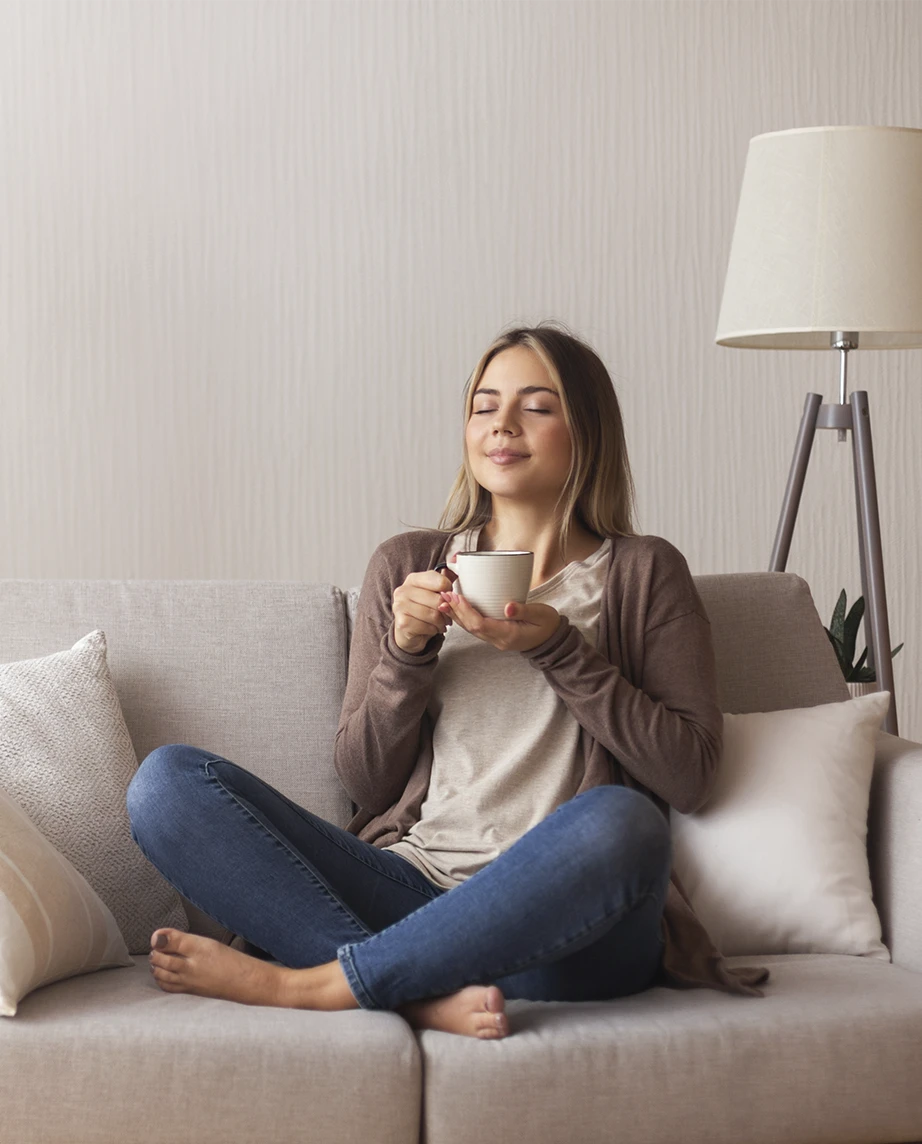 woman sitting cross-legged on the sofa, holding a cup, with a calm expression