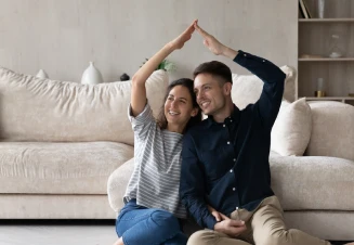 Casal sentado no chão, a sorrir e a fazer forma de casa com os braços