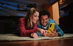 Casal jovem, deitados no chão, a mexer no telemóvel