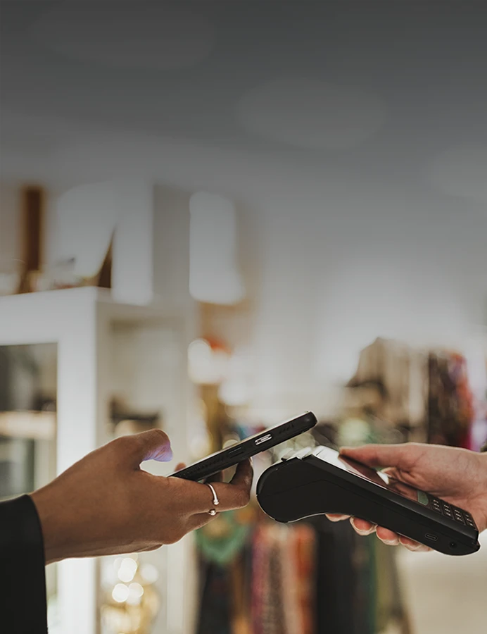 mão de comerciante a segurar TPA e mão de cliente com telemóvel a fazer pagamento